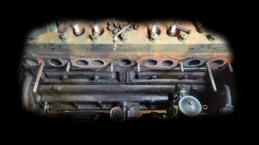 Close-up of an old, rusty engine part with visible bolts and spark plugs.