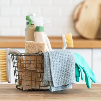 Cleaning supplies including brushes, gloves, and sprays in a wire basket.