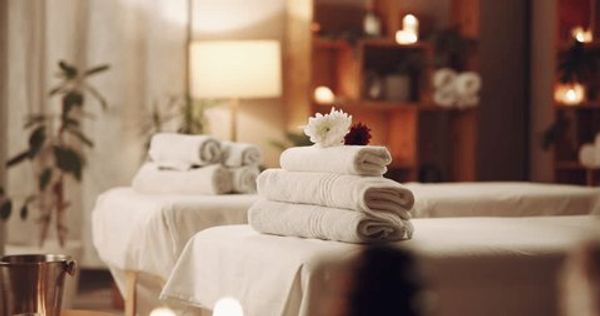 Stacked white towels with flowers on massage tables in a cozy spa room.