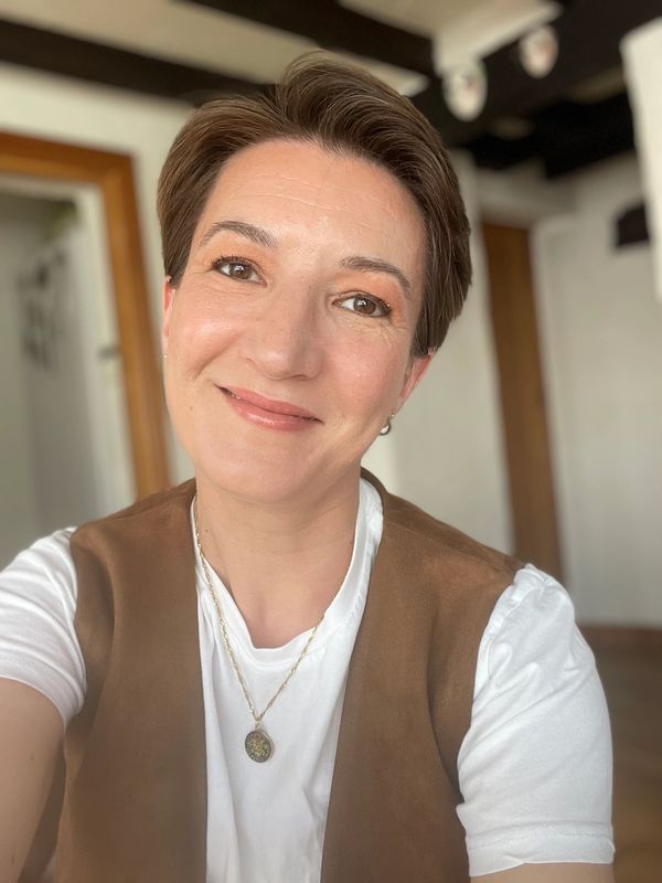 Smiling woman with short hair wearing a white shirt and brown vest.