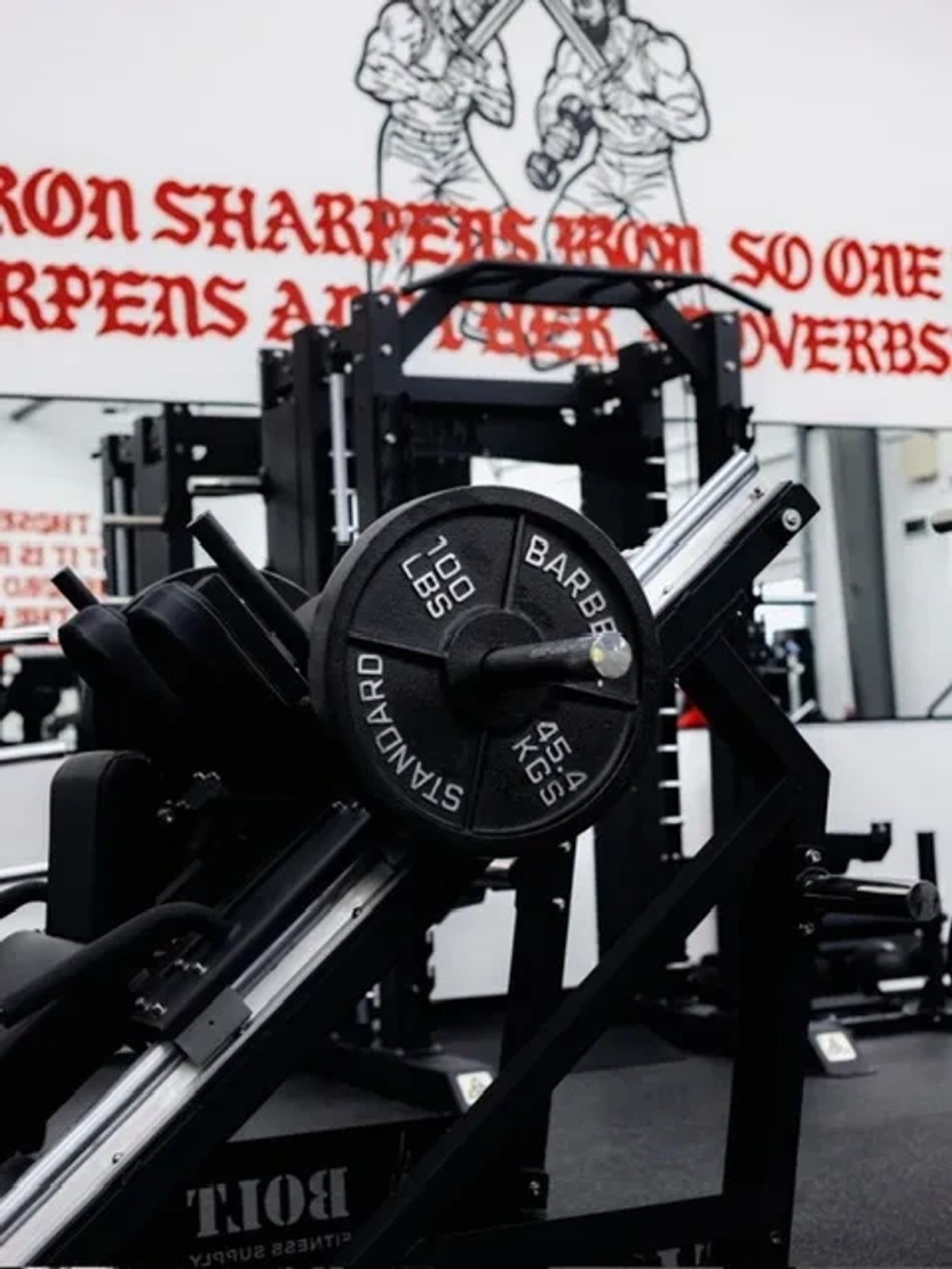 Weightlifting equipment with 100 lbs plates in a gym setting.