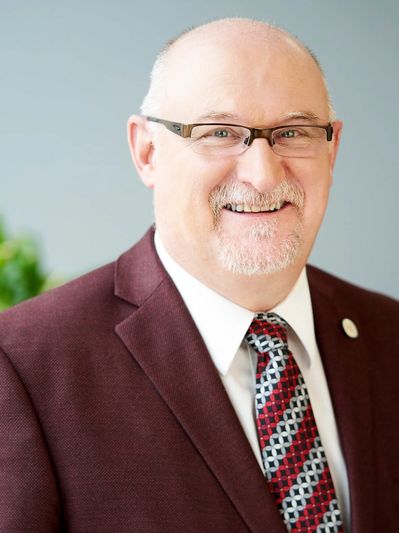 Smiling man in glasses and maroon suit jacket.