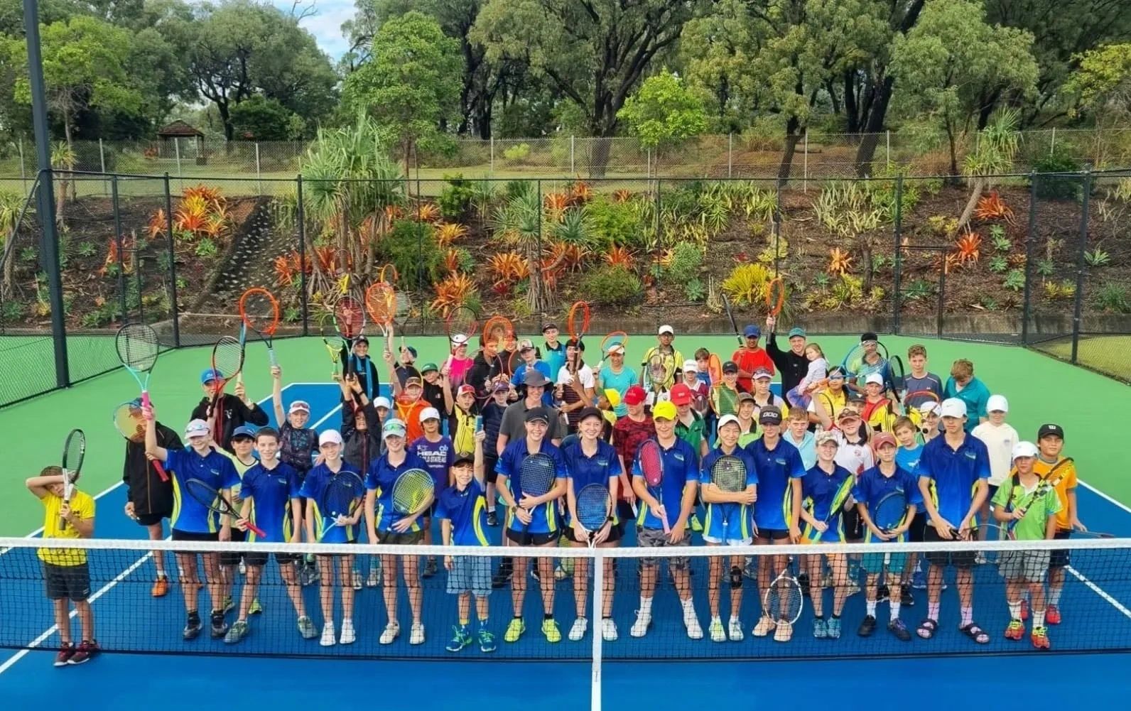 Large group of young tennis players on court holding racquets.