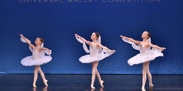 Three young ballerinas in white tutus performing on stage.