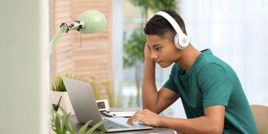 African-American teenage boy with headphones using laptop at table in room