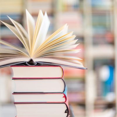 Stack of books with one open book on top in a library setting.