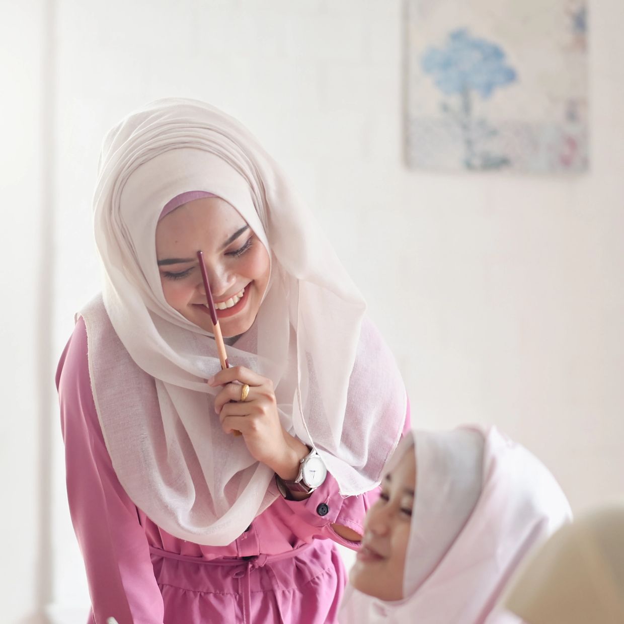 Two women in hijabs sharing a joyful moment indoors.