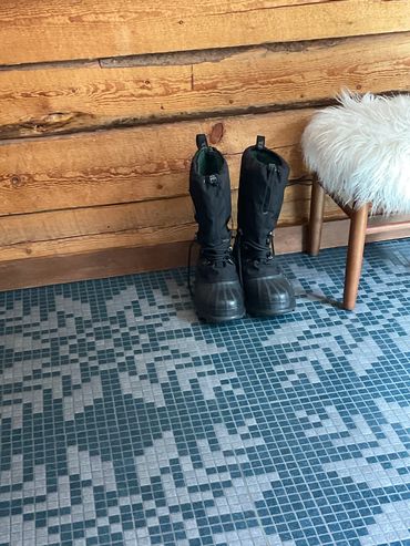 Mosaic tile floor featuring large snowflakes, with winter boots and wood stool in log cabin