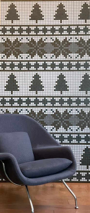 Nordic mosaic mural with repeating patterns of pine trees and snowflakes behind armchair