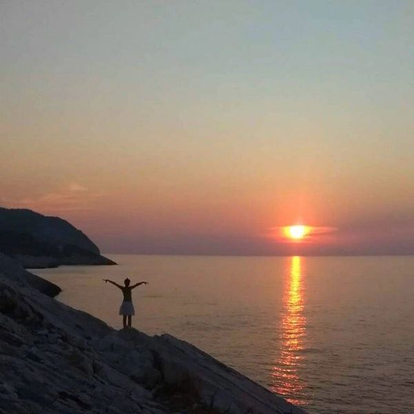junge Frau Arme ausgebreitet stehend auf Felsen am Strand bei Sonnenuntergang Insel Vis in Kroatien