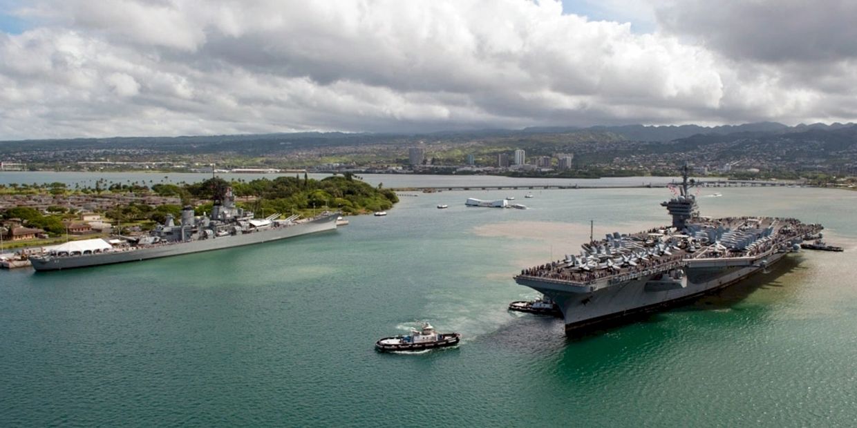 Two large naval ships docked with tugboats in a harbor.