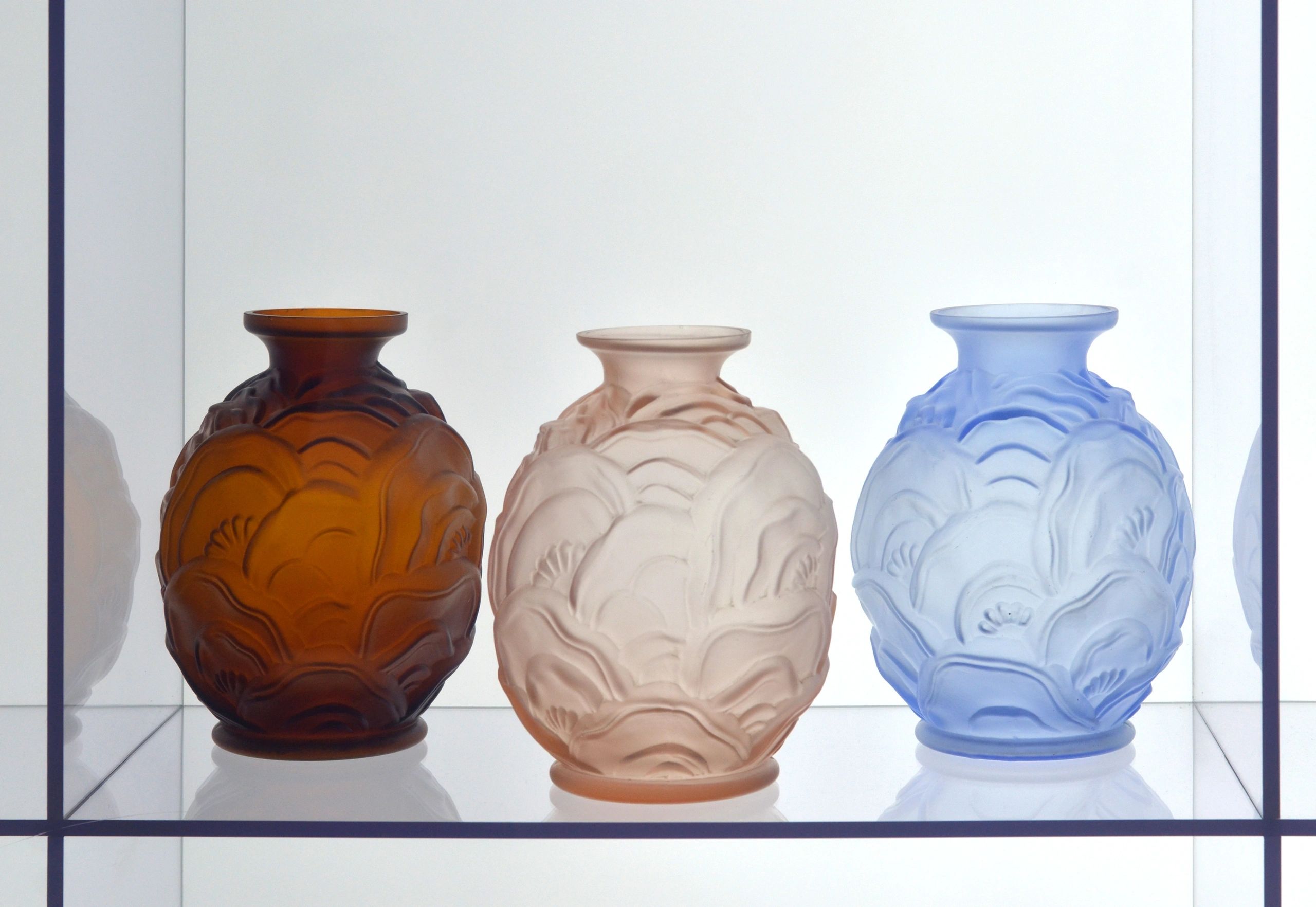 A trio of Art Deco molded art glass vases with organic floral forms in amber, peach, and sky blue.