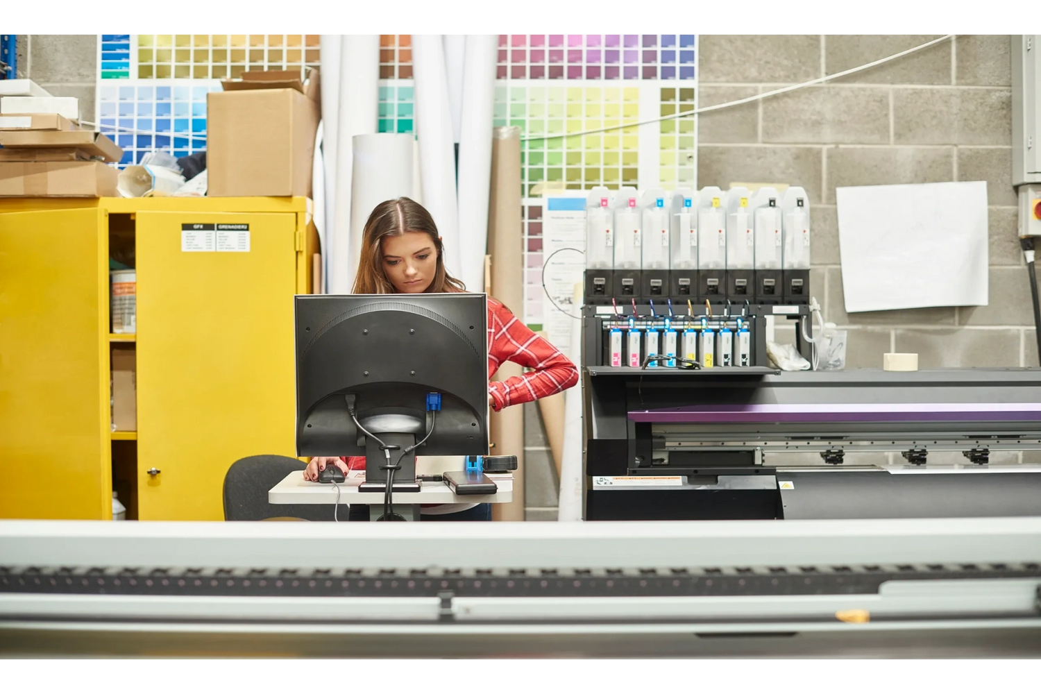 Woman working at computer in a printing workshop with color samples on the wall.