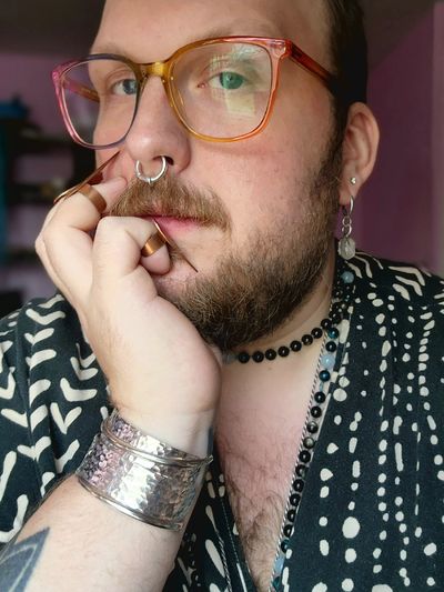 Person with colorful glasses, jewelry, and detailed patterned clothing.