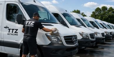 Worker detailing a fleet of white Mercedes vans under a sunny sky.