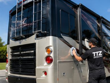 A man detailing the side of a large black and silver RV.