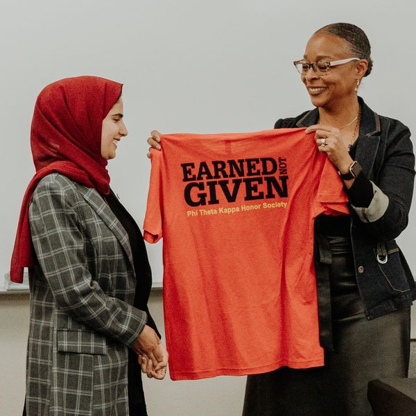 Two women, one holding a red shirt that says Earned Not Given.