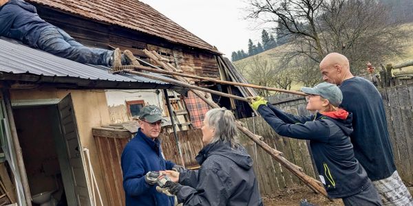 Group working together to repair a wooden roof on a rustic building.