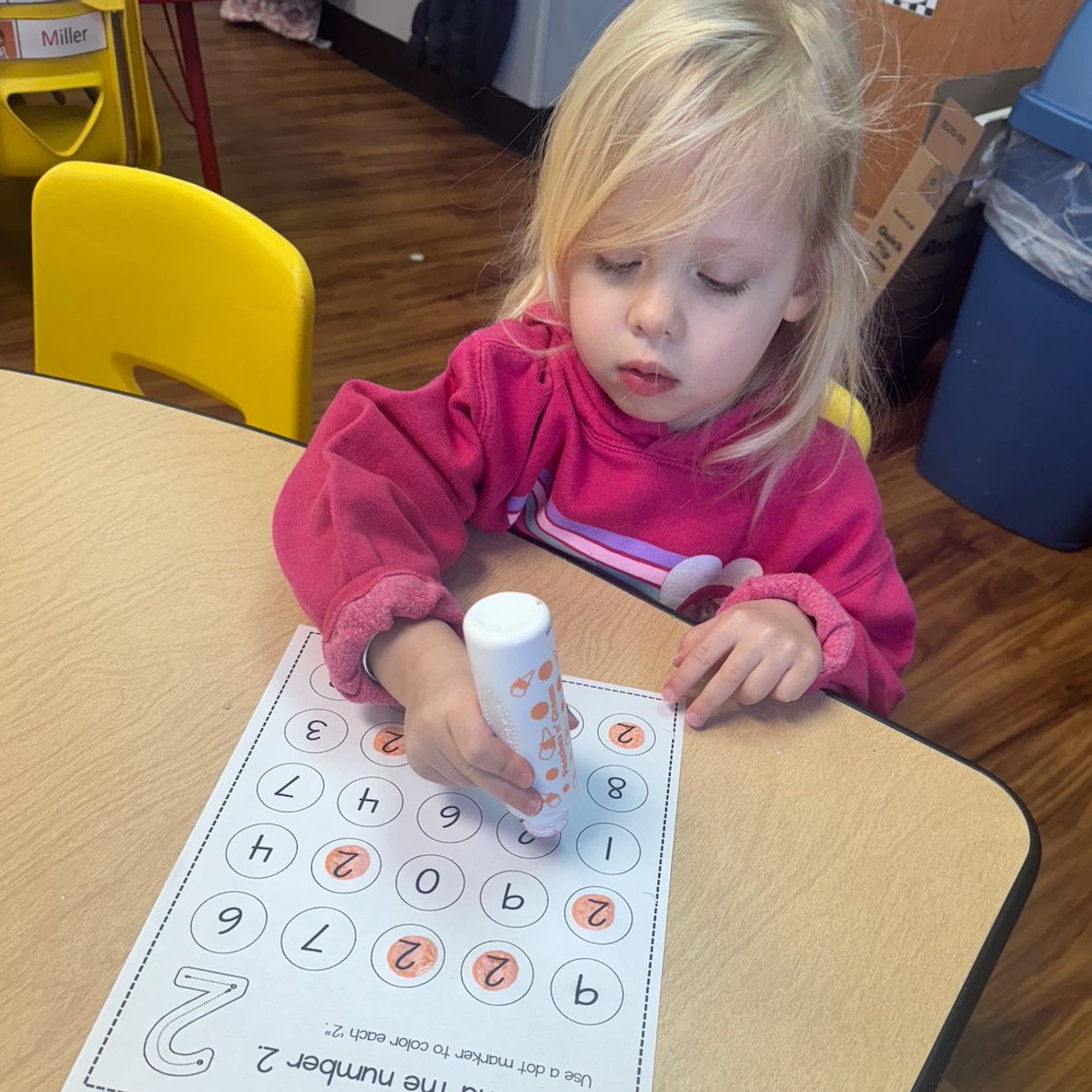 A young girl colors number 2 on a worksheet using a dot marker.