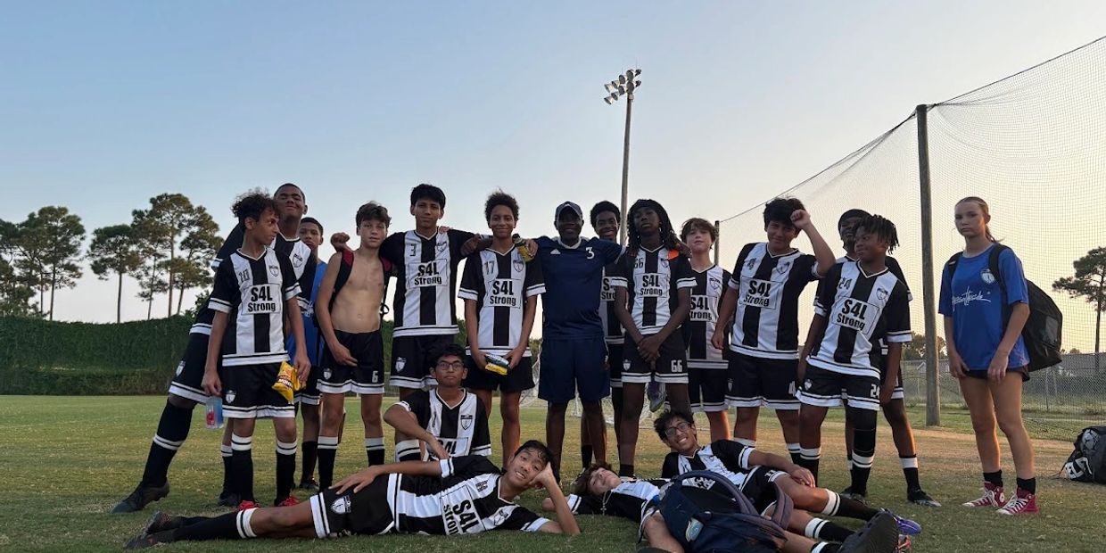 Youth soccer team in black and white uniforms posing on a field at dusk.