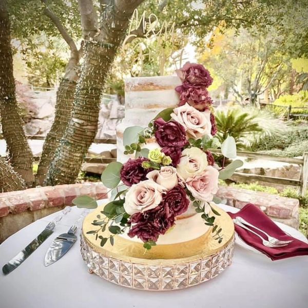 Elegant two-tiered wedding cake adorned with pink and burgundy flowers outdoors.