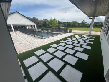 Modern backyard with a pool, safety fence, and stepping stones on artificial grass.