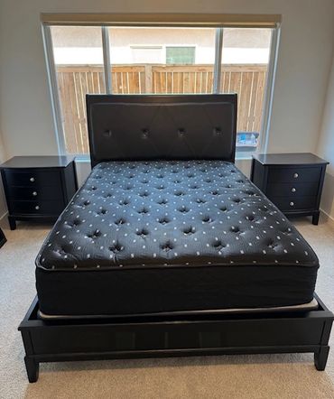 Black bed with mattress and two matching nightstands in front of a large window.