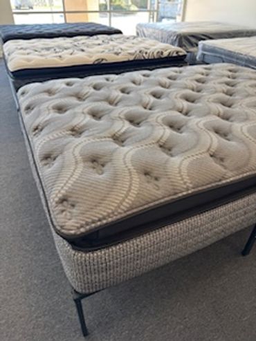 Several mattresses displayed in a showroom, with a close-up on a tufted mattress.