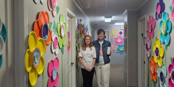 Two people standing in a colorfully decorated hallway with flower art on the walls.