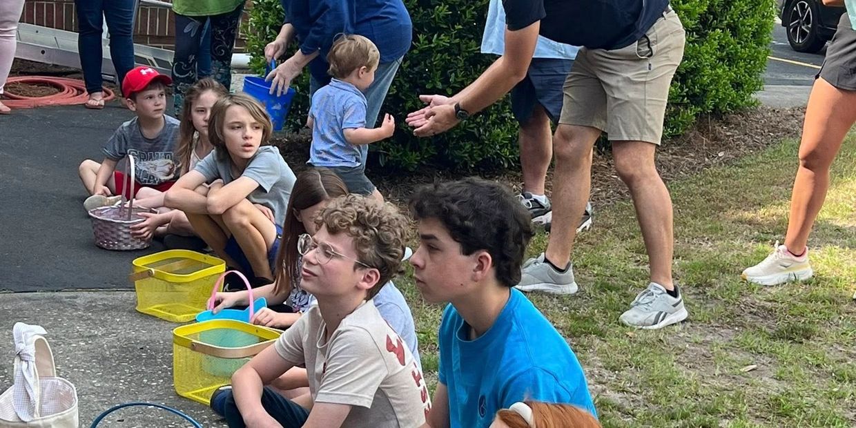 Group of children and adults gathered outdoors with colorful baskets, interacting and observing.
