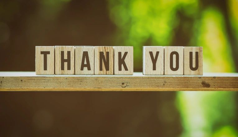 Blocks spell out 'THANK YOU' on a wooden surface.