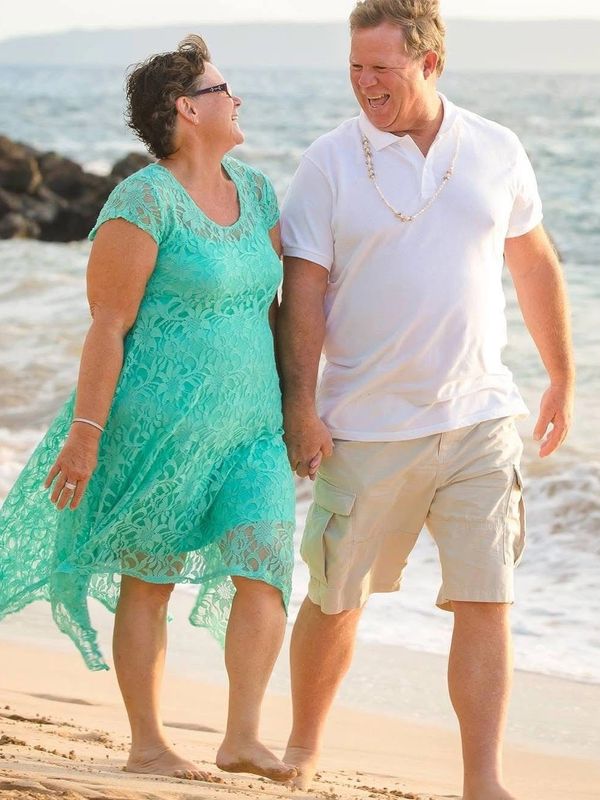 Couple holding hands walking on the beach, smiling.