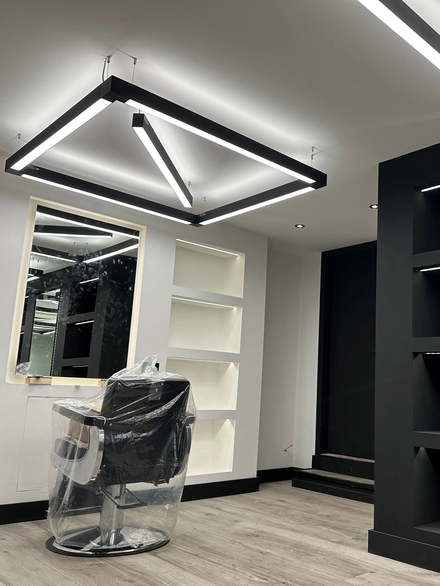 Modern barbershop interior with LED lighting and a barber chair covered in plastic.
