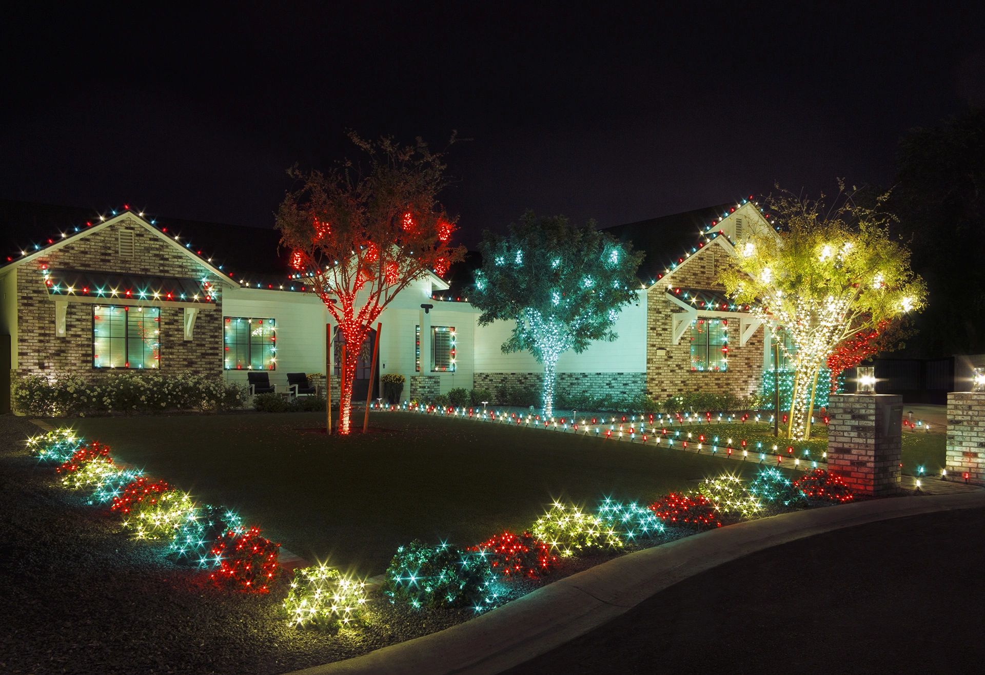 House and yard decorated with colorful Christmas lights at night.