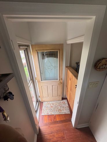 Open wooden door with decorative glass and floral mat inside a home entryway.