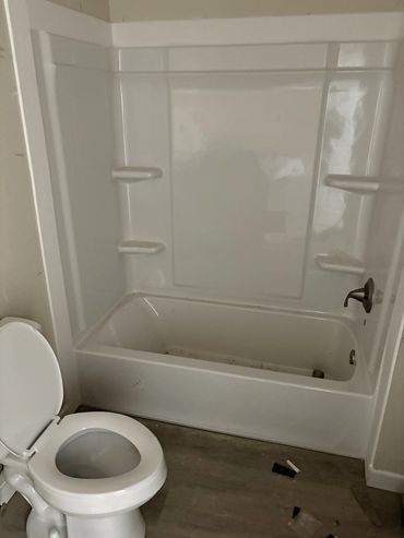 Small bathroom with a bathtub and toilet, showing some dirt and debris on the floor.