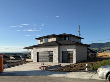 Modern two-story house under construction with a spacious driveway and garage doors.