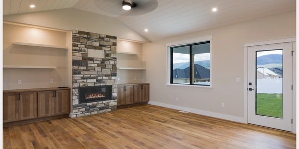 Modern living room with hardwood floors, stone fireplace, and large window with mountain view.