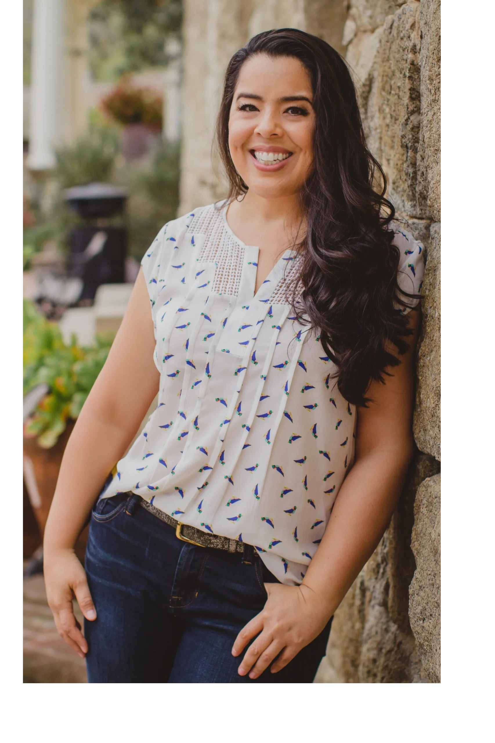 Dr. Monarrez, a smiling woman with long, dark hair, leaning against a stone wall.