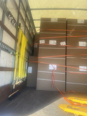 Boxes secured with orange straps inside a truck with yellow cargo control straps hanging on the side.