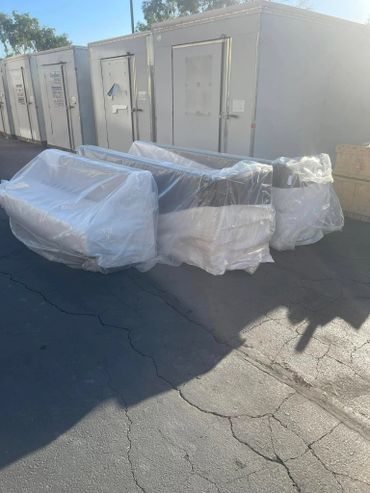 Three wrapped couches outside near storage units on cracked pavement.