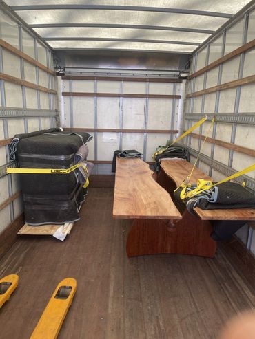 Wooden furniture pieces secured inside a moving truck with protective blankets and straps.