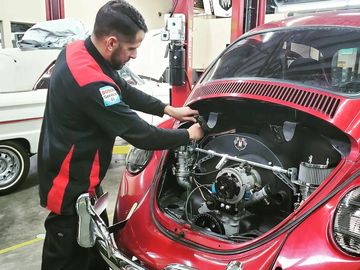 Mechanic working on the engine of a red VW bug.