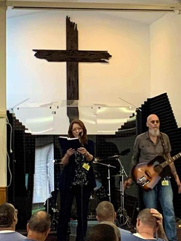 Woman reading from a book in front of a cross in a church.
