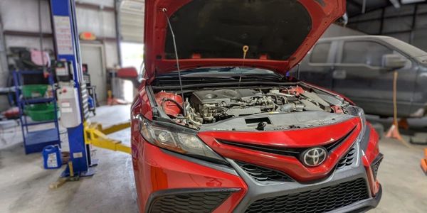 Red Toyota car with open hood in a garage for repair.
