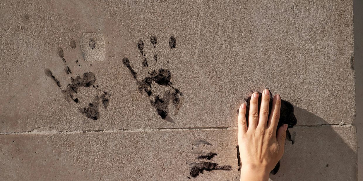 A hand pressing on a wall making a black handprint beside two other handprints.