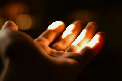 Close-up of a hand illuminated by warm light in darkness.