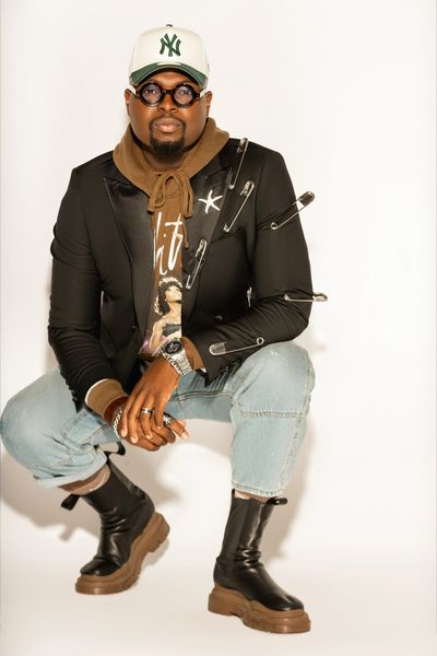 Man wearing a black blazer with large safety pins, jeans, and boots.