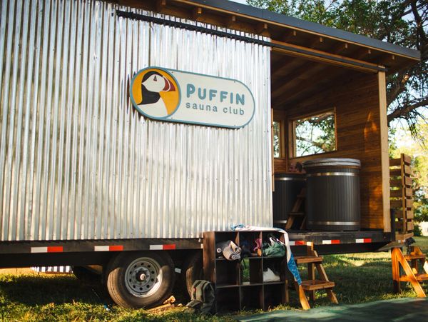 Mobile sauna club with wooden barrels and storage cubbies outside in a grassy area.