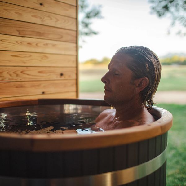 Man relaxing in an outdoor wooden hot tub with eyes closed.